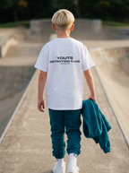 Child wearing a white t-shirt with text at a skate park