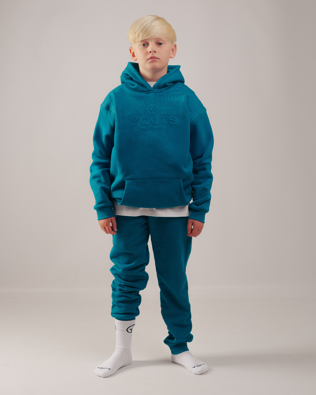 Person wearing a teal hoodie and pants set on a plain background